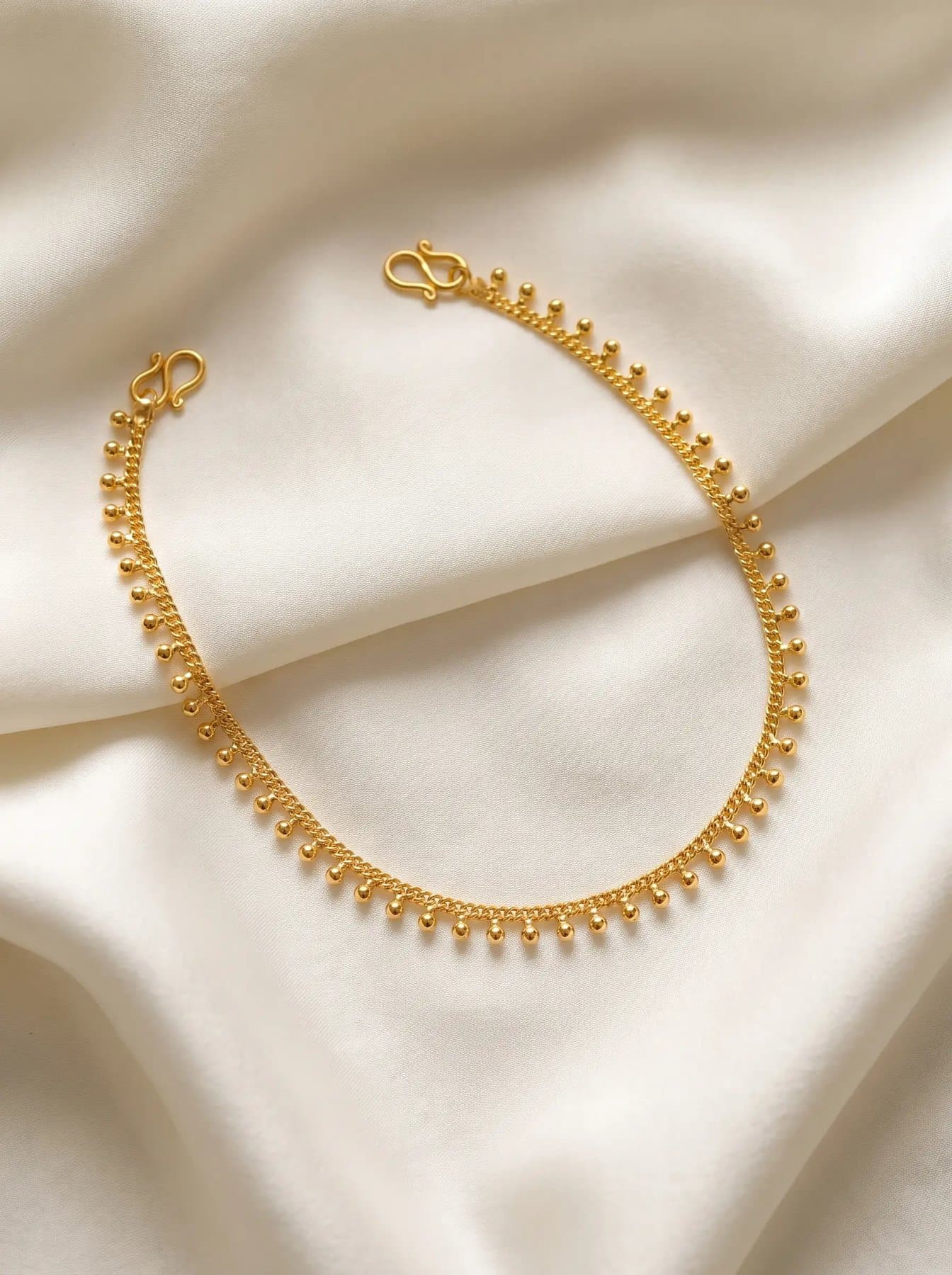 Delicate gold anklet with tiny bead drops laid on ivory silk