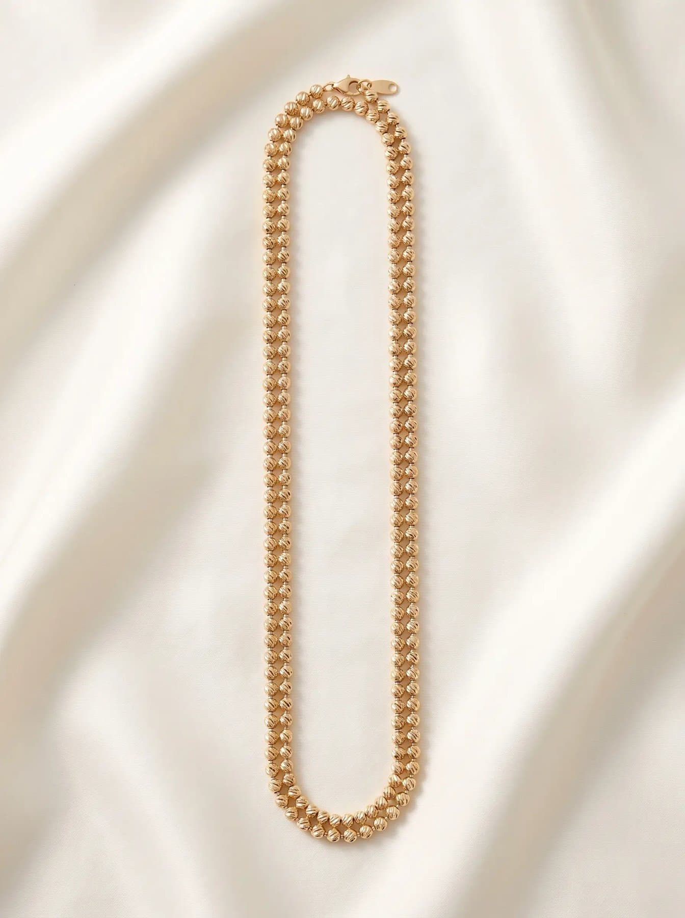 Long double strand of fine round gold beads coiled on ivory silk