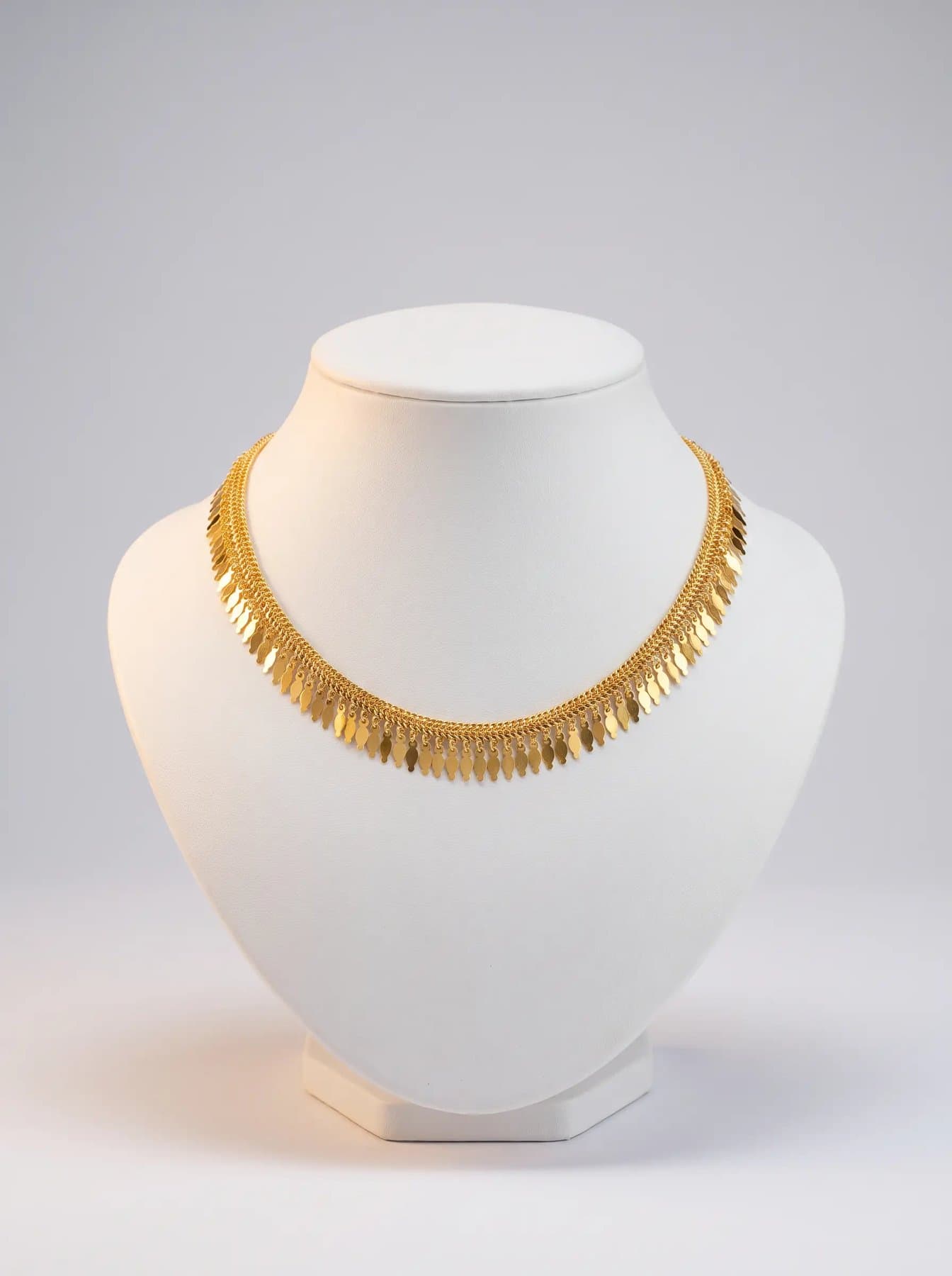 Woven chain collar with a dense fringe of gold leaf drops on a white display bust