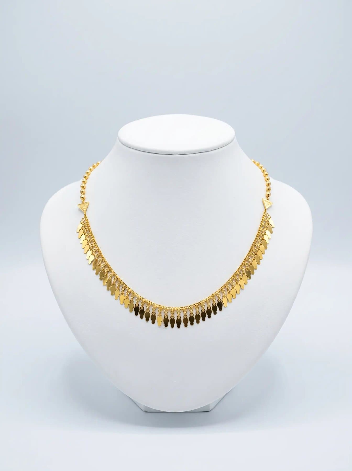 Fringe necklace hung from twin triangular clasps on a white display bust