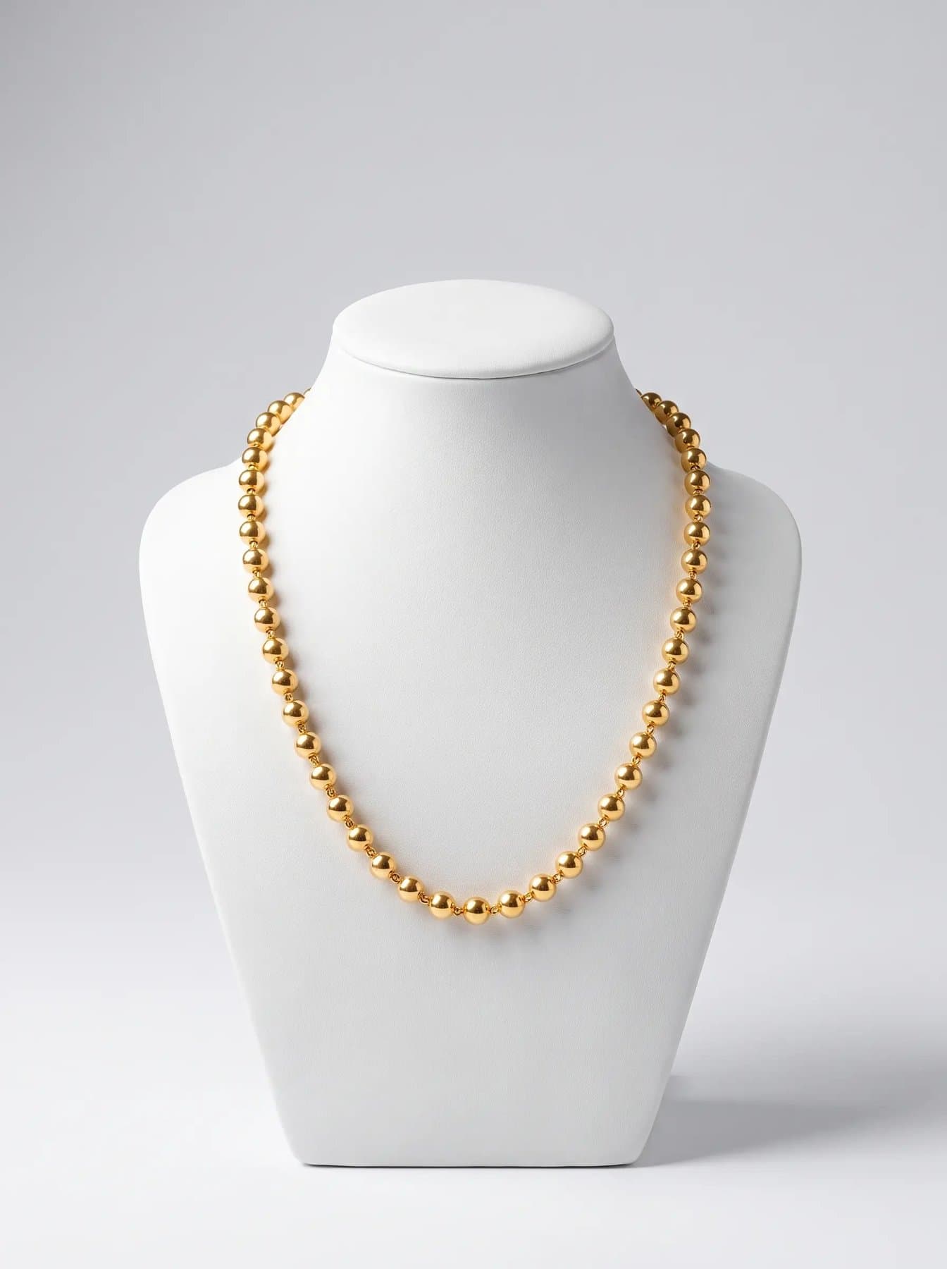 Classic mala of round polished gold beads on a white display bust