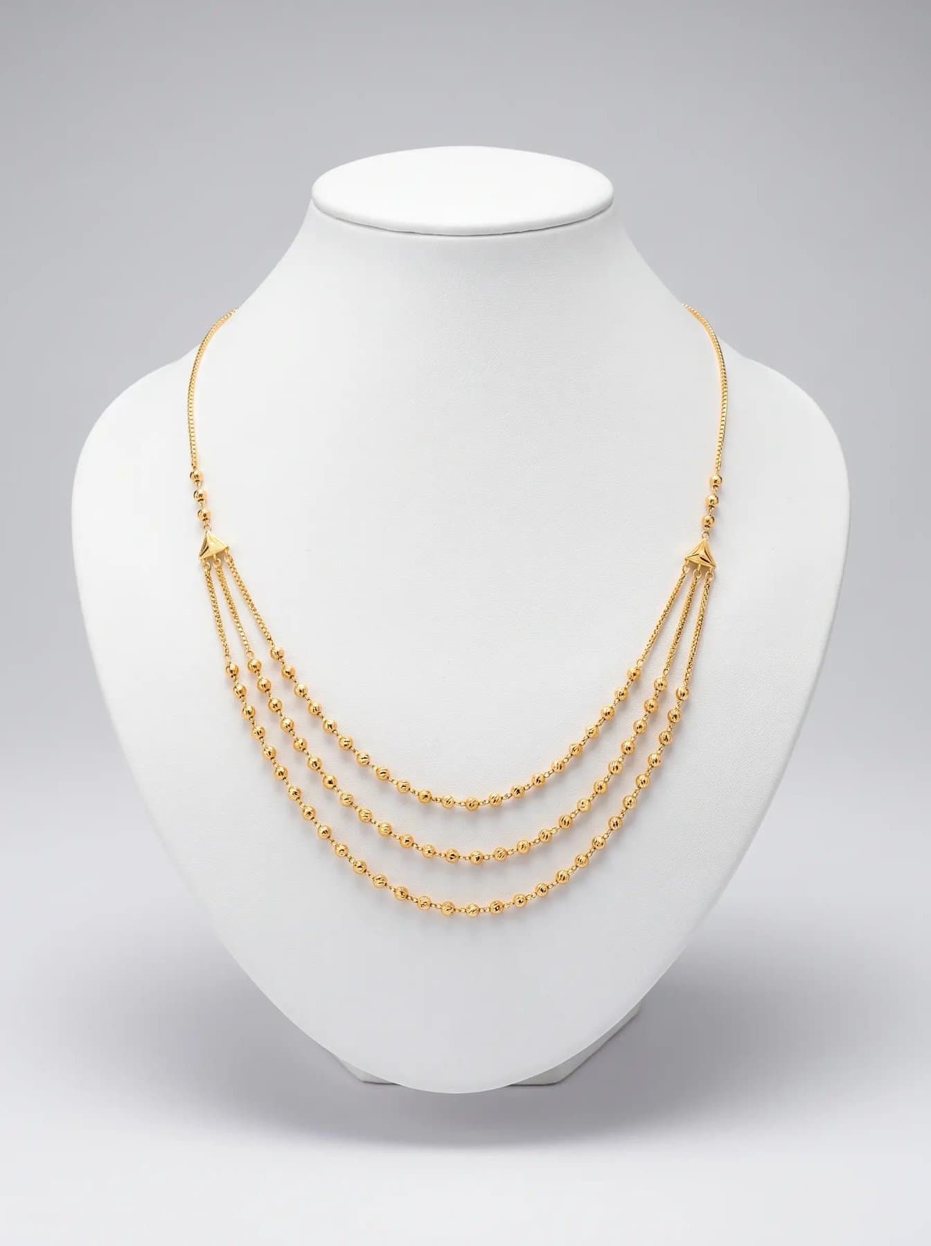 Three layered strands of fine gold beads on a white display bust