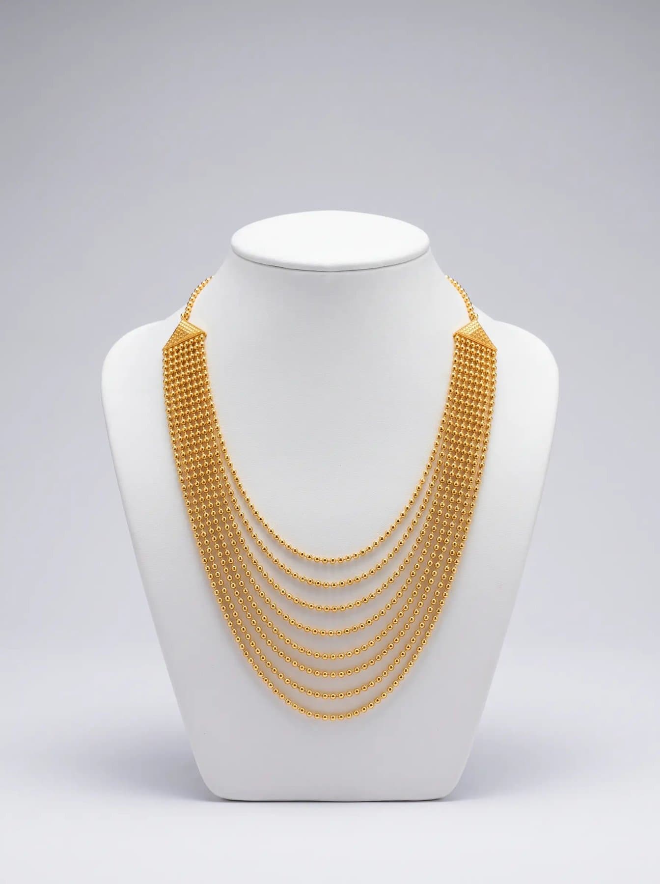 Nine falling strands of fine gold beads from pyramid clasps on a white display bust