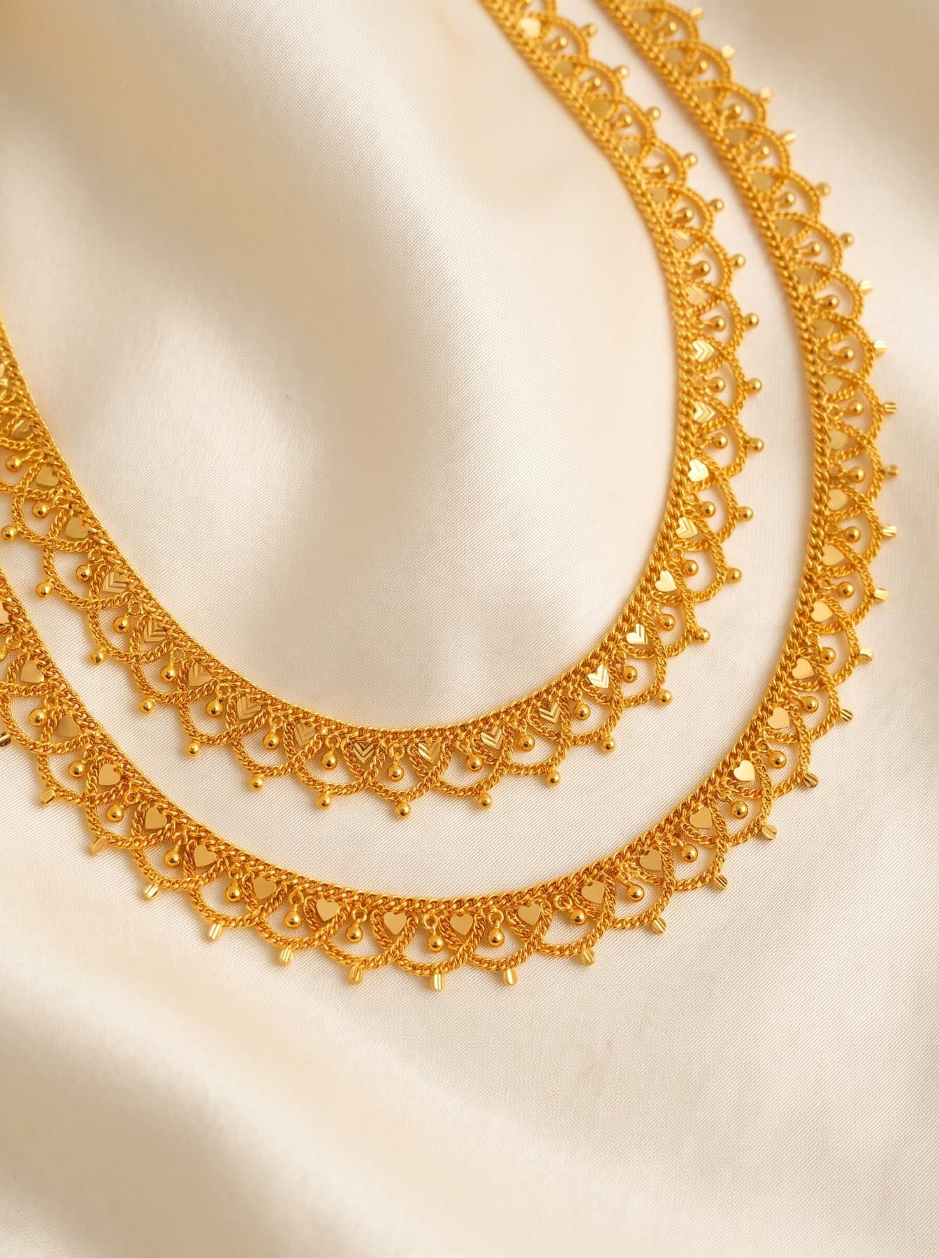 Pair of scalloped gold lace chains laid in curves on ivory silk