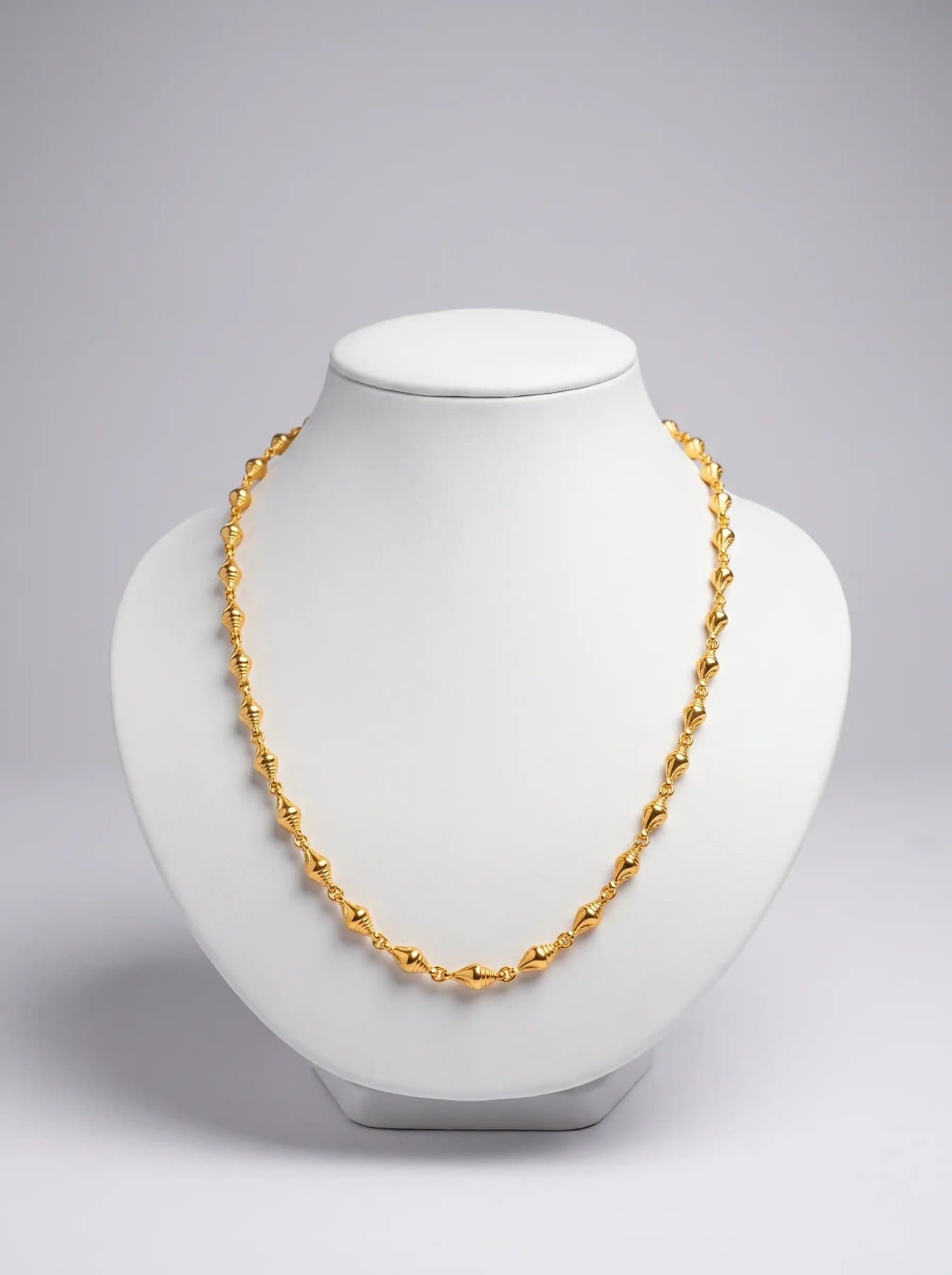 Gold chain of elongated fluted spiral beads on a white display bust