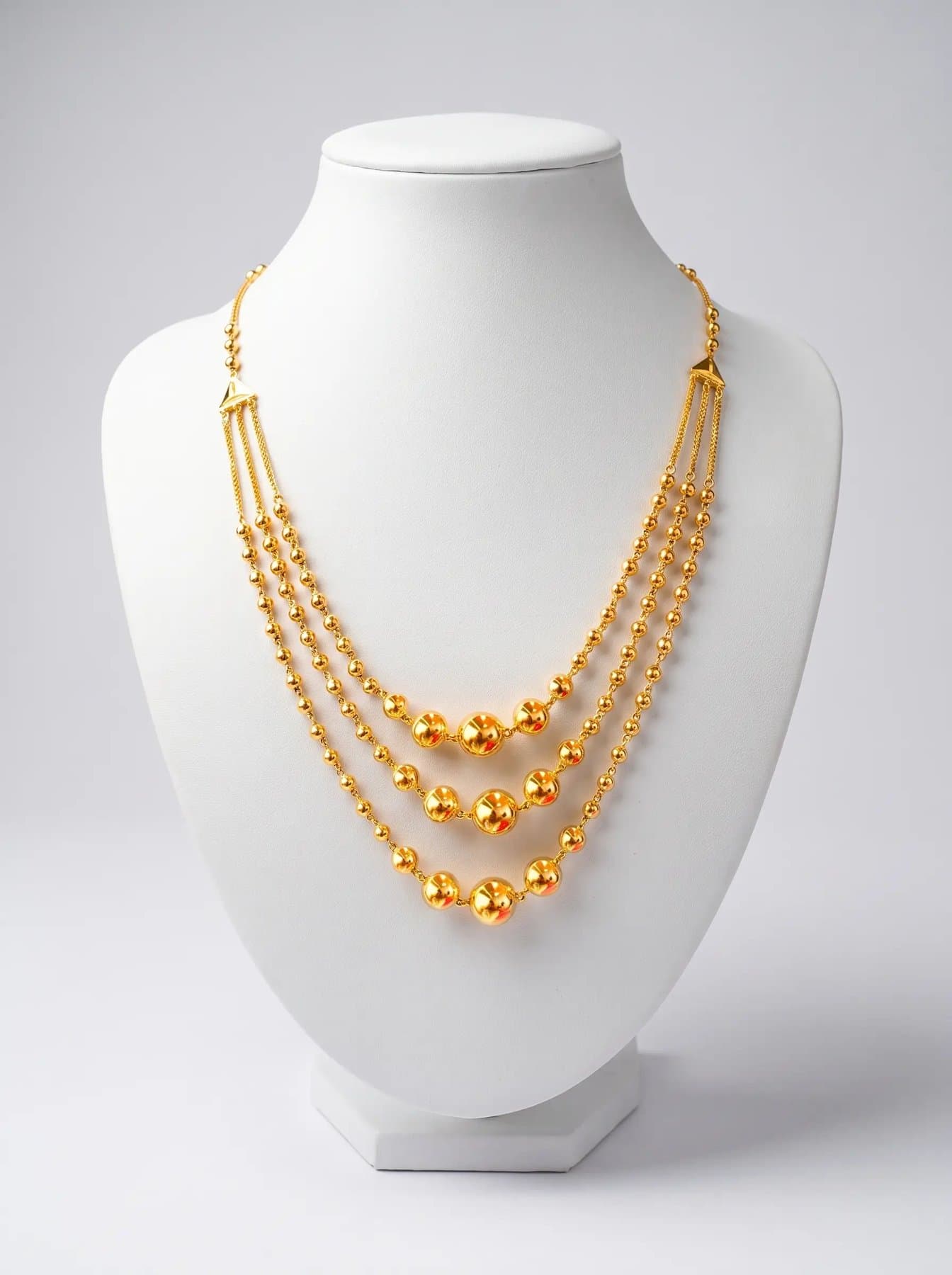 Three graduated strands of polished gold beads draped on a white display bust
